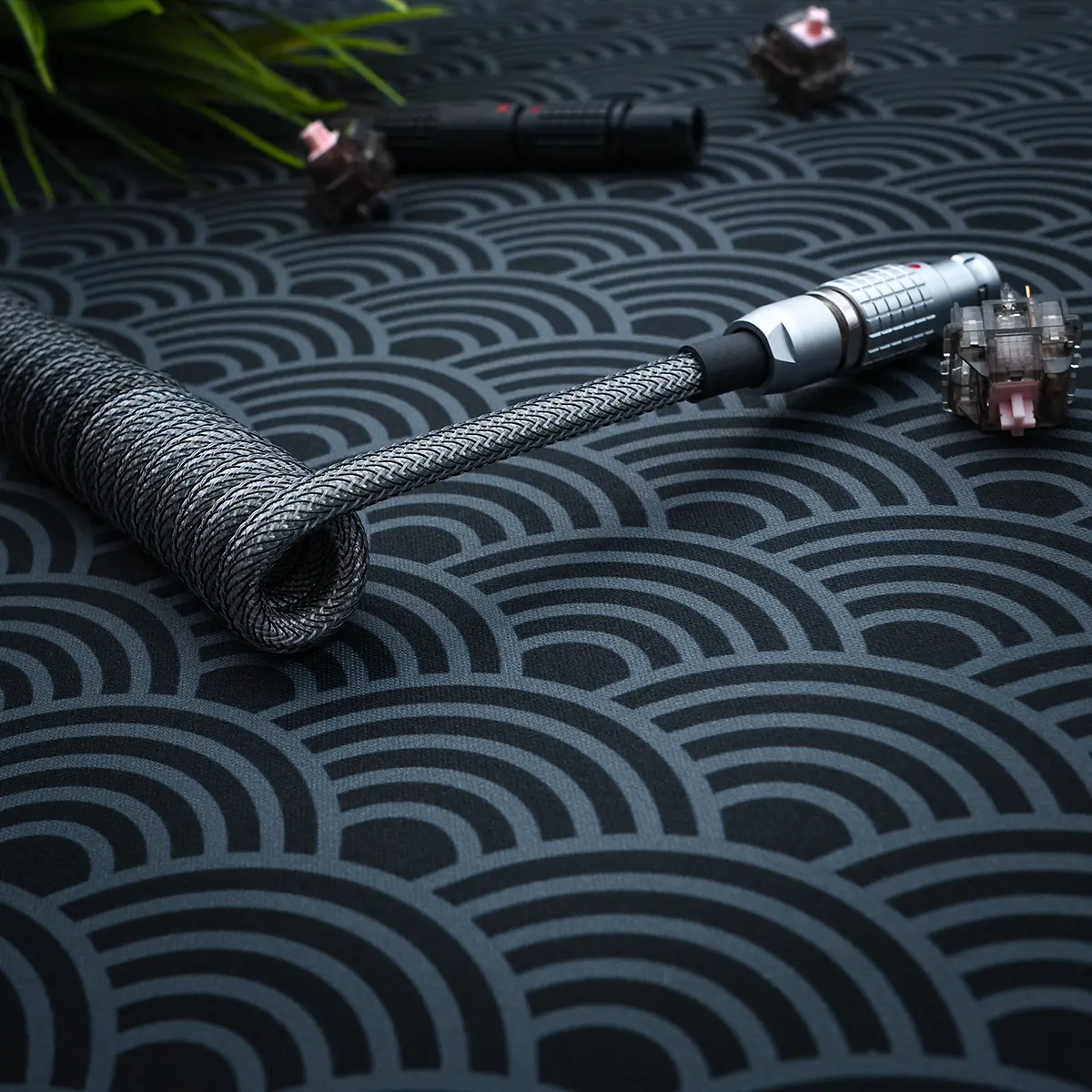 Coiled dark gray keyboard cable featuring a sleek braided design and detachable connectors. The metal housing adds durability, perfect for custom setups.