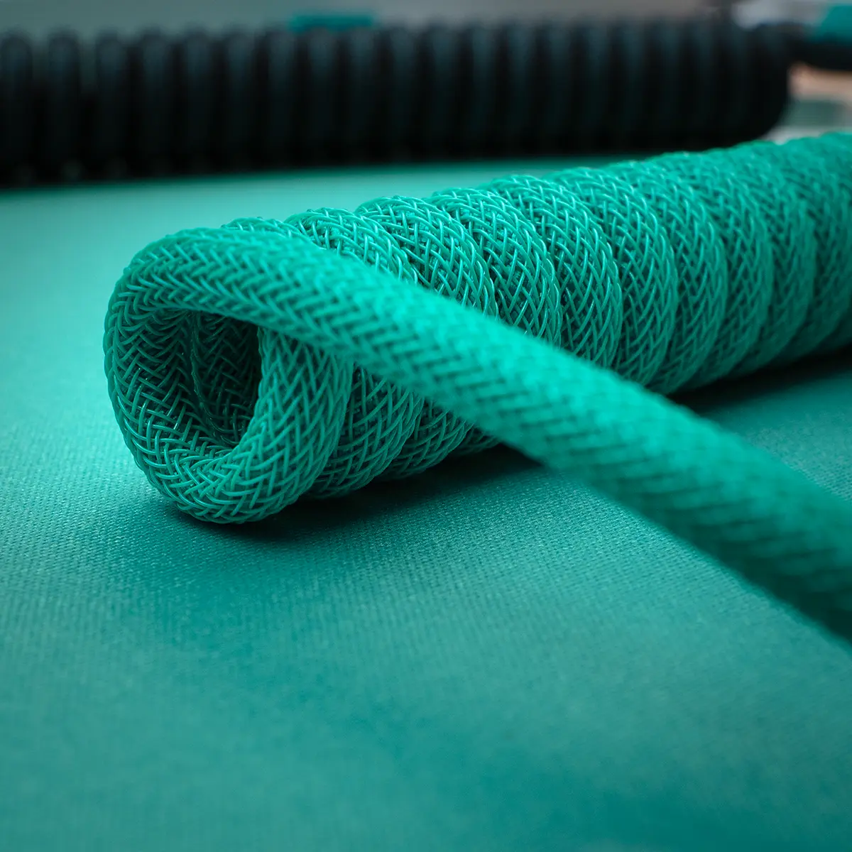 A vibrant teal coiled keyboard cable showcasing intricate braiding and a smooth finish, ideal for custom setups, emphasizing style and durability.