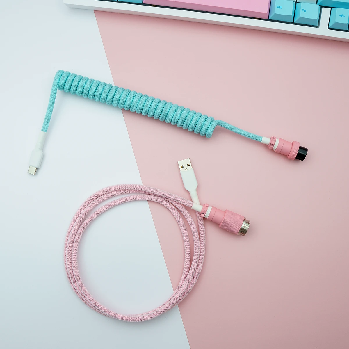 Custom keyboard cable features a coiled aqua blue section and a straight pink part. It includes USB-C and aviator connectors, showcasing quality braiding.