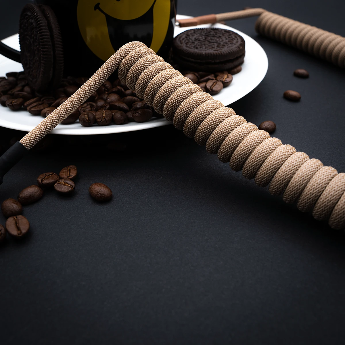Coiled beige paracord keyboard cable with a sleek finish, featuring a detachable connector for easy customization, surrounded by coffee beans.