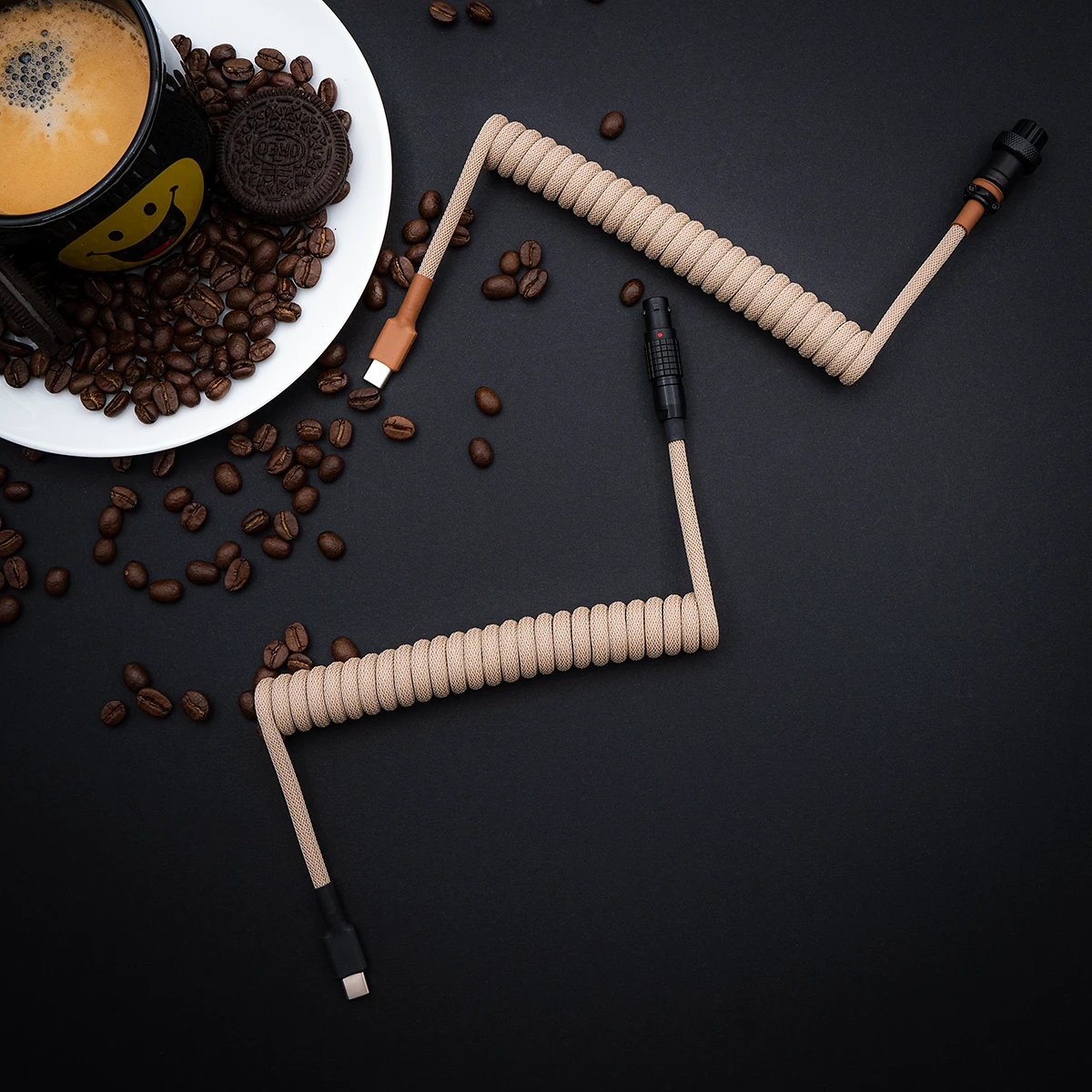 Coiled beige paracord keyboard cable with USB-C and aviator connectors, featuring high-quality braiding and a sleek finish amidst coffee beans.
