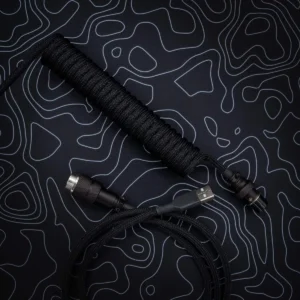 Coiled black keyboard cable with braided paracord finish, featuring USB-C and aviator connectors, showcasing high-quality CNC metal housing and heatshrink.