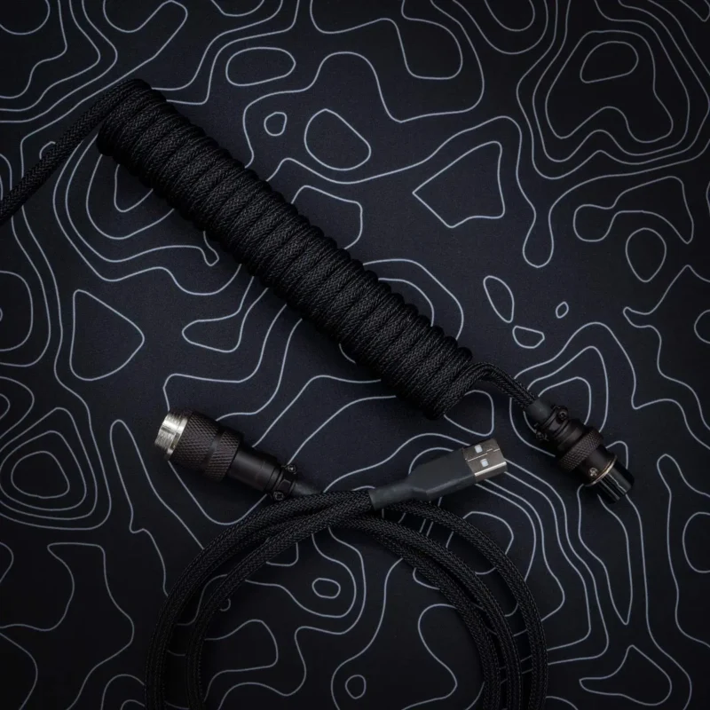 Coiled black keyboard cable with braided paracord finish, featuring USB-C and aviator connectors, showcasing high-quality CNC metal housing and heatshrink.