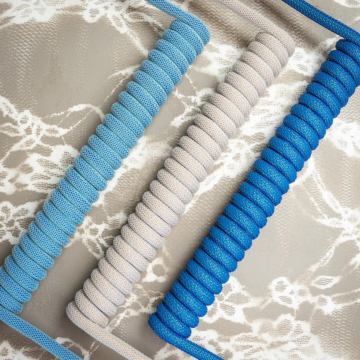 Custom keyboard cables showcased in blue and gray braiding, featuring a prominent coil design, high-quality finish, and detachable connectors.