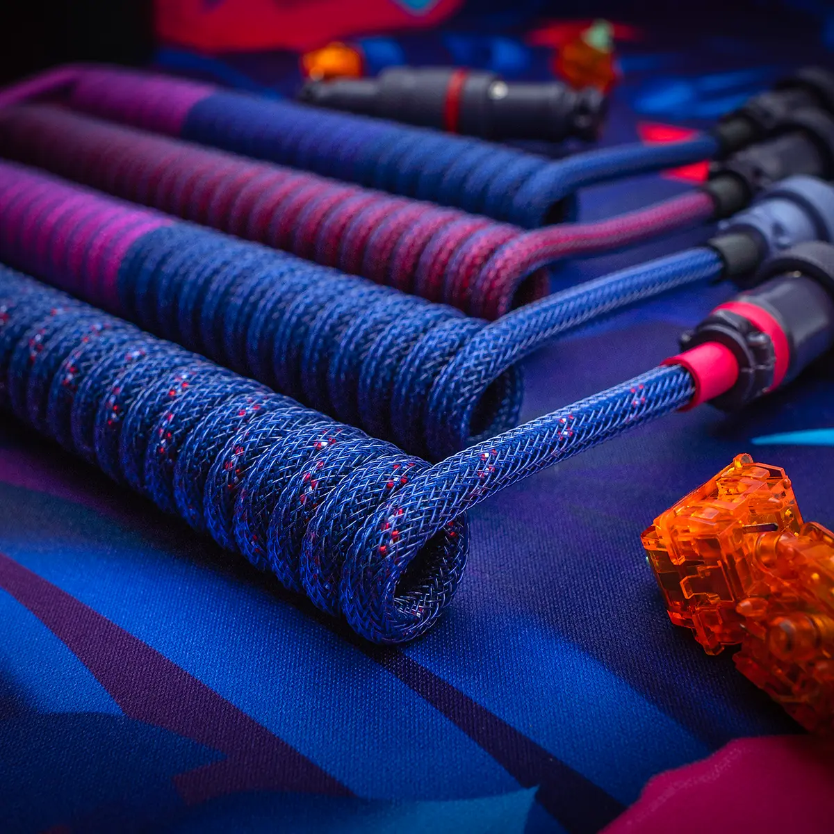A close-up of the GMK Laser Keyboard Cable showcases a colorful braided design with coils in various lengths, featuring detachable USB-C and aviator connectors.