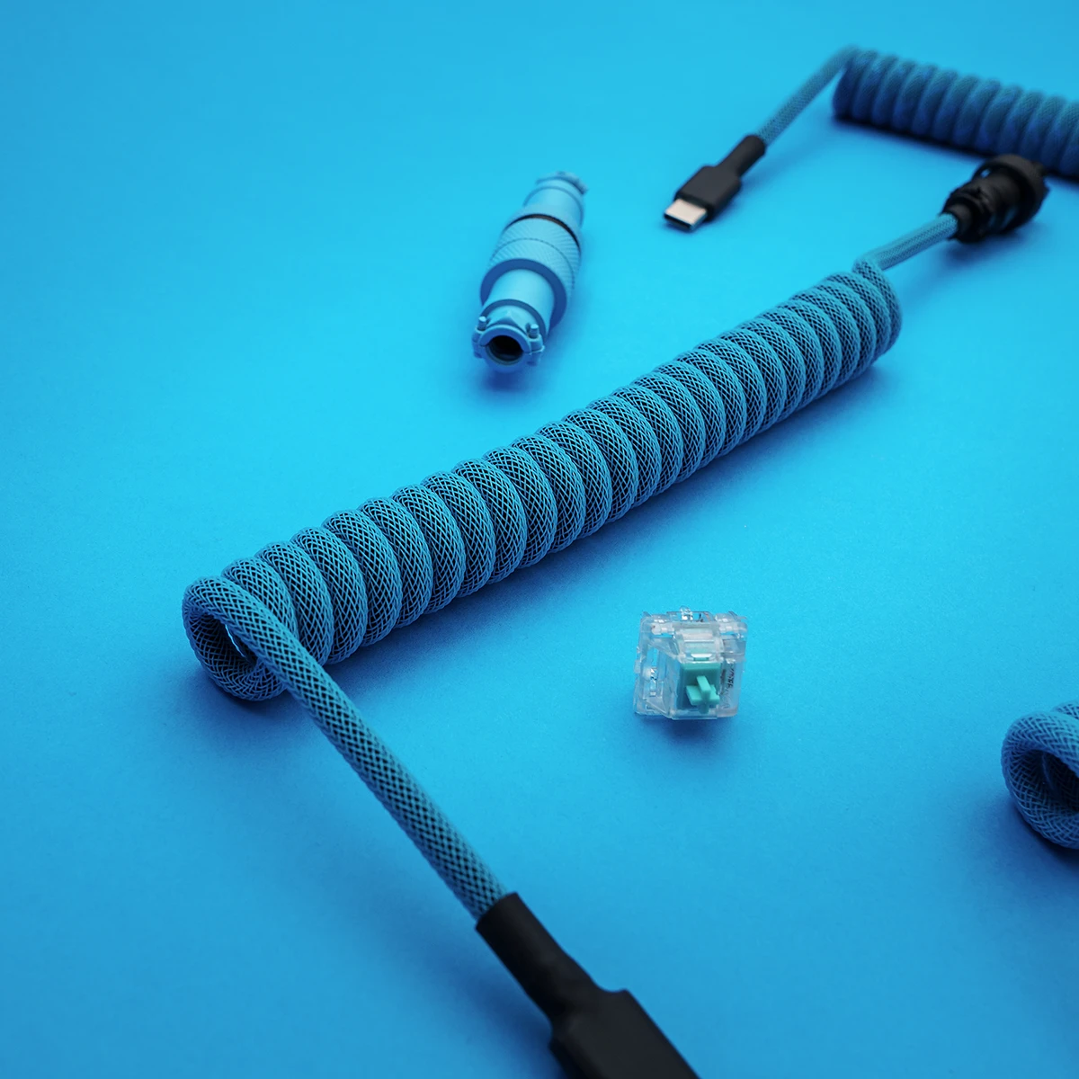 A vibrant blue paracord keyboard cable features a coiled design, detachable USB-C connector, and CNC metal housing for quality and durability.