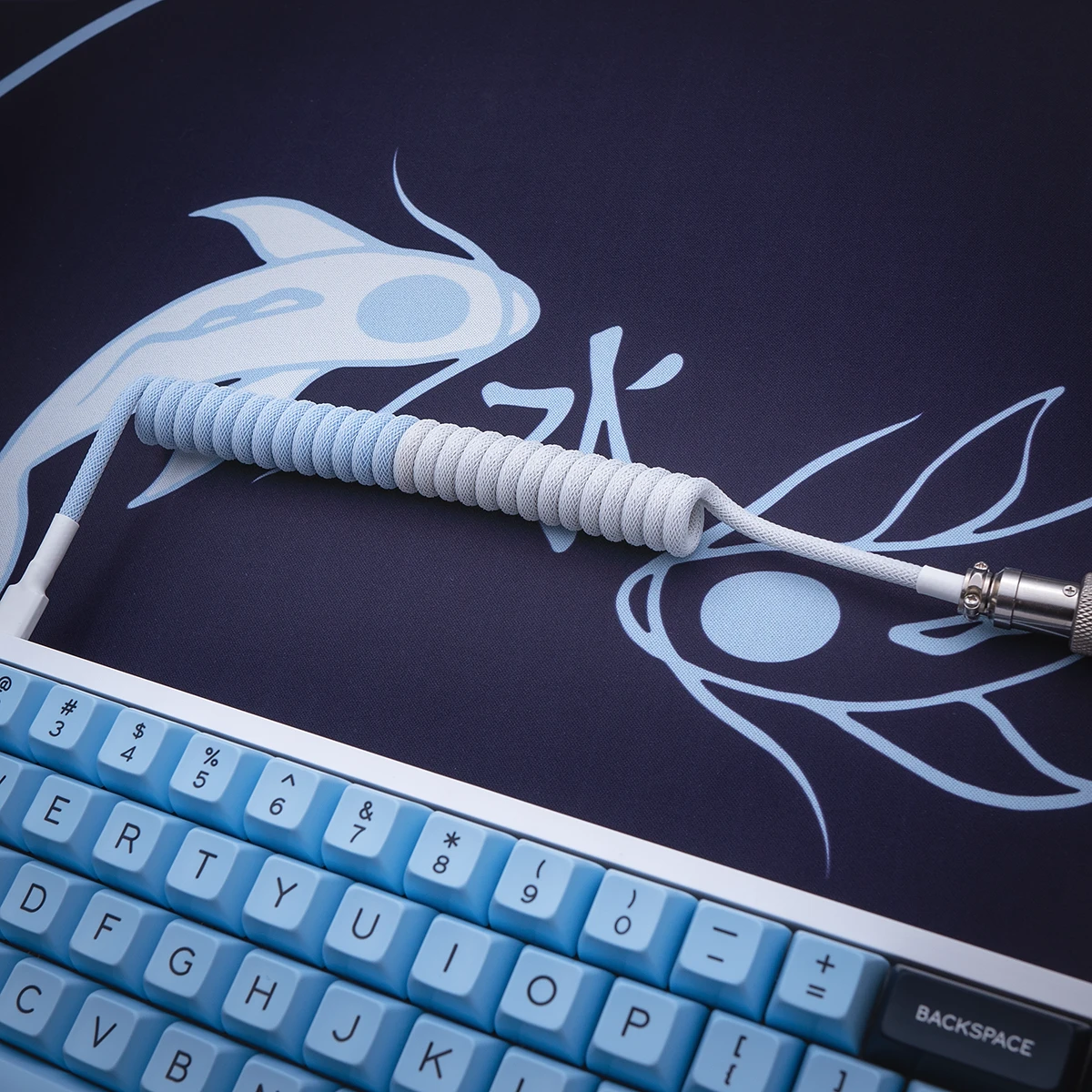 Coiled keyboard cable in blue and white paracord, featuring detachable connectors and high-quality metal housing, showcasing a sleek, textured finish.