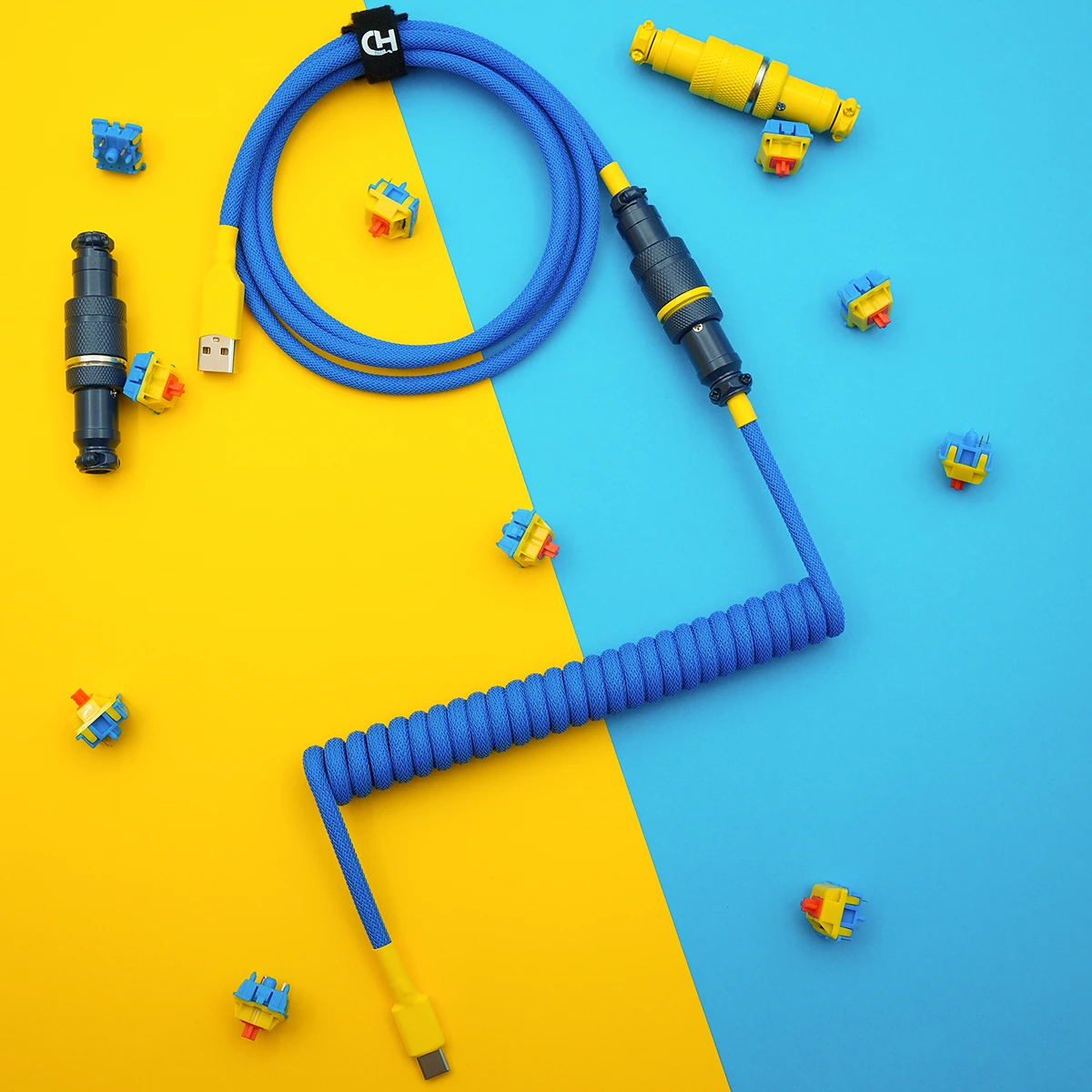 A vibrant blue coiled keyboard cable featuring USB-C and detachable aviator connectors, surrounded by colorful key switches. Ideal for custom setups.