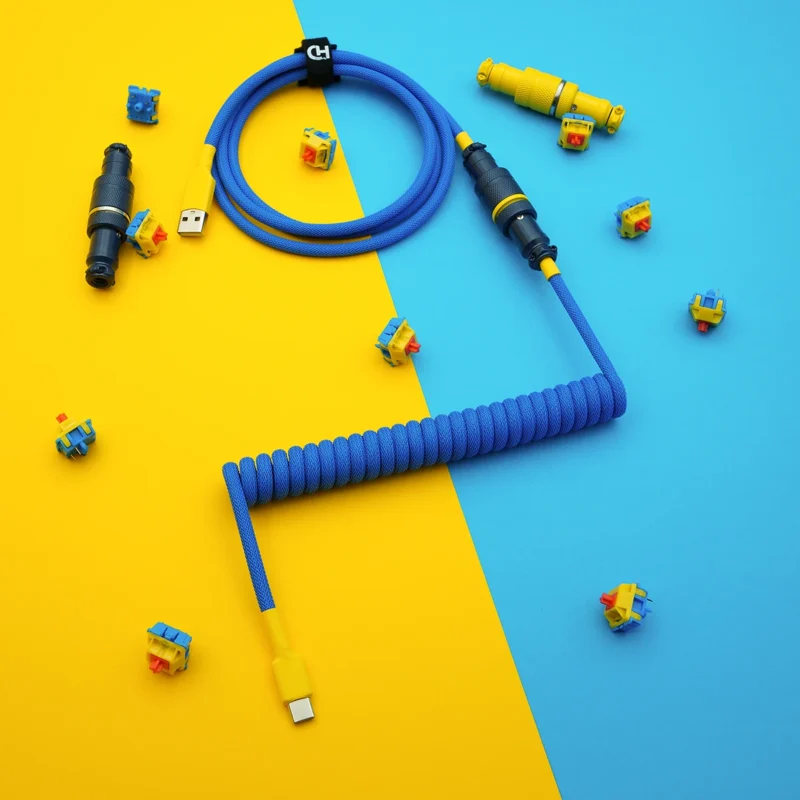 Bright blue custom keyboard cable featuring a coiled design, detachable yellow USB-C and aviator connectors, with high-quality paracord braiding and CNC metal housing.