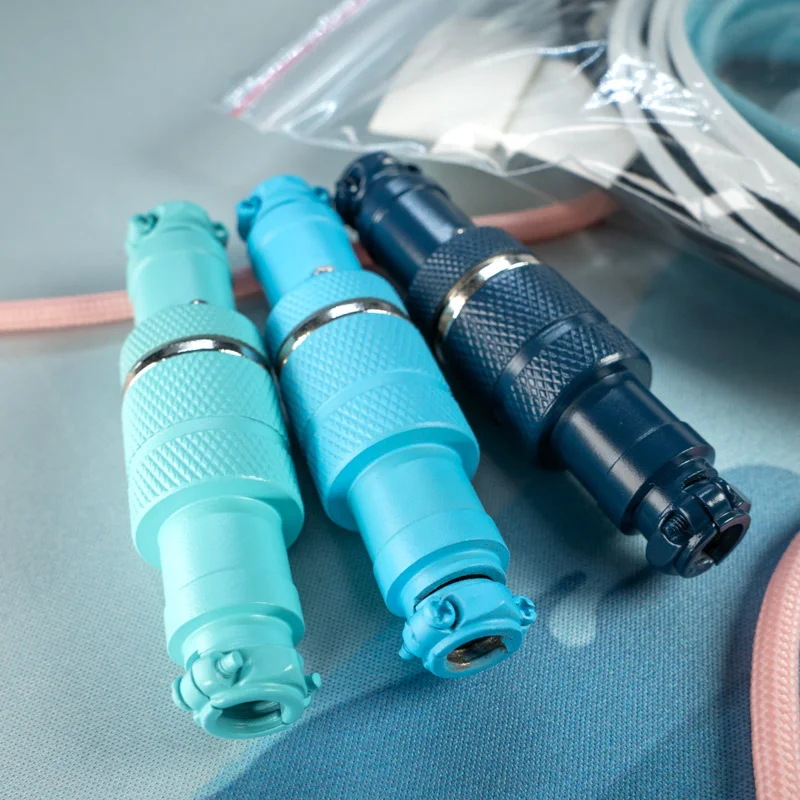 Three metal gx16 4 pins aviators connectors with a Cerakote finish in different shades of blue are arranged side by side on a light blue surface.