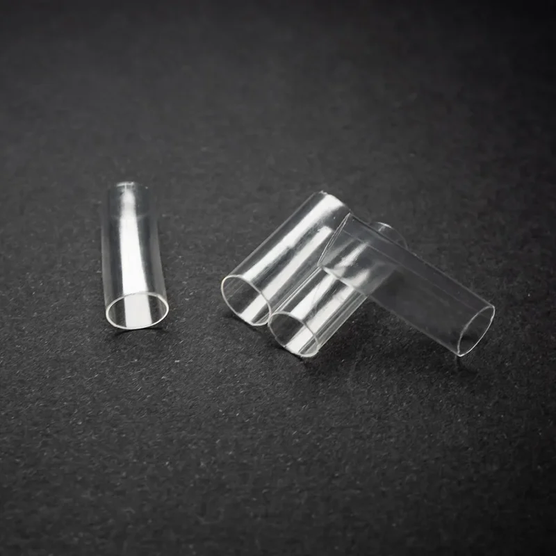 Four Clear Heatshrink (6.5mm) – (1/4) transparent plastic tubes are lying on a black surface, with three grouped together and one separated to the left.