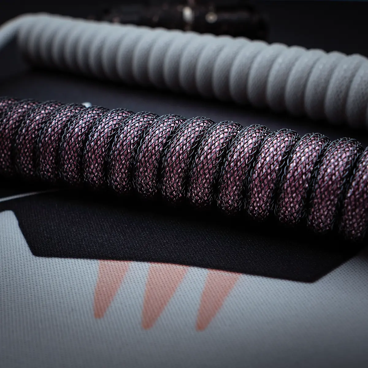 Coiled black and pink paracord keyboard cables, showcasing a textured finish. Features include detachable connectors and a durable quality ideal for custom setups.