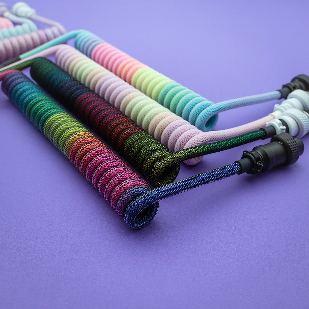 A vibrant selection of coiled keyboard cables in various colors, featuring detachable connectors and textured paracord braiding for durability.