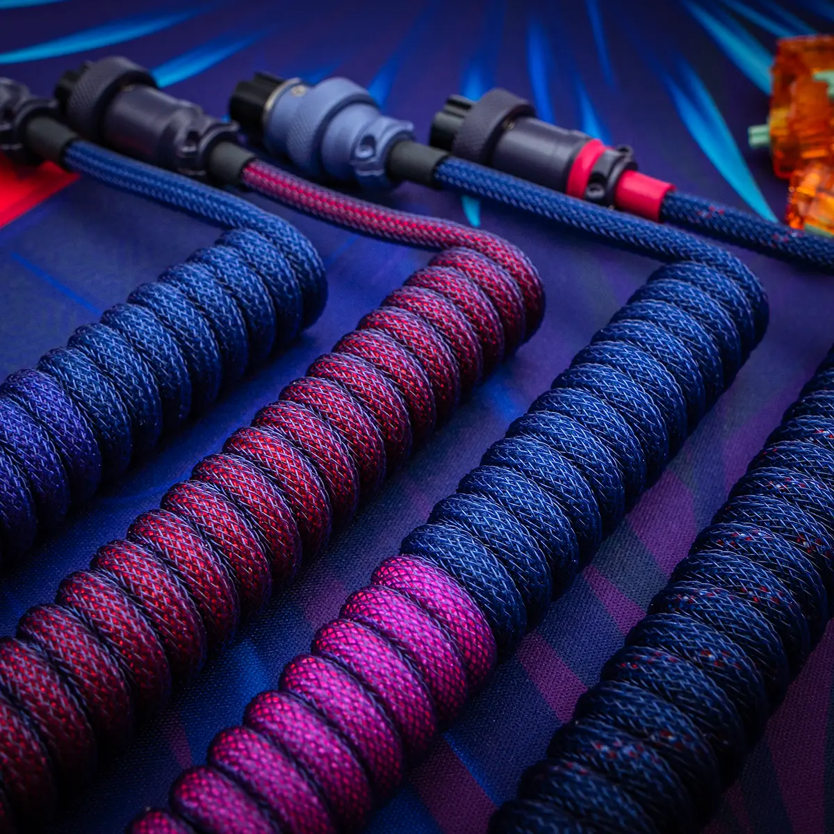Custom keyboard cables showcasing vibrant paracord braiding in red, blue, and purple. Features detachable connectors in various styles for versatility.