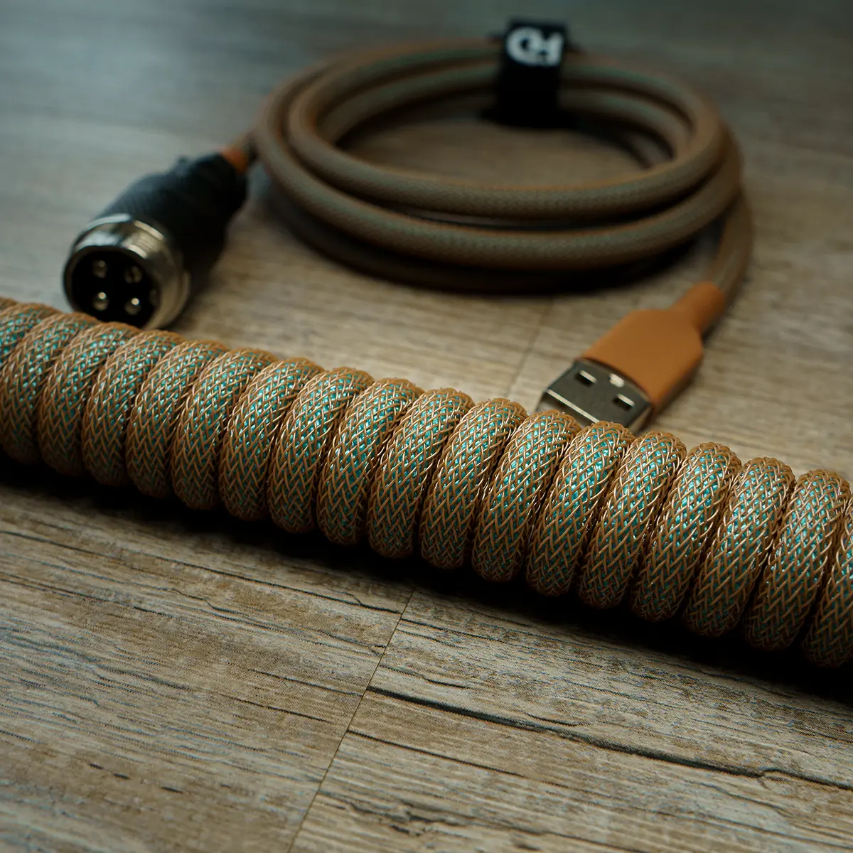 Coiled GMK Copper keyboard cable with a braided gold and green paracord finish, featuring a USB connector and CNC metal housing for durability.