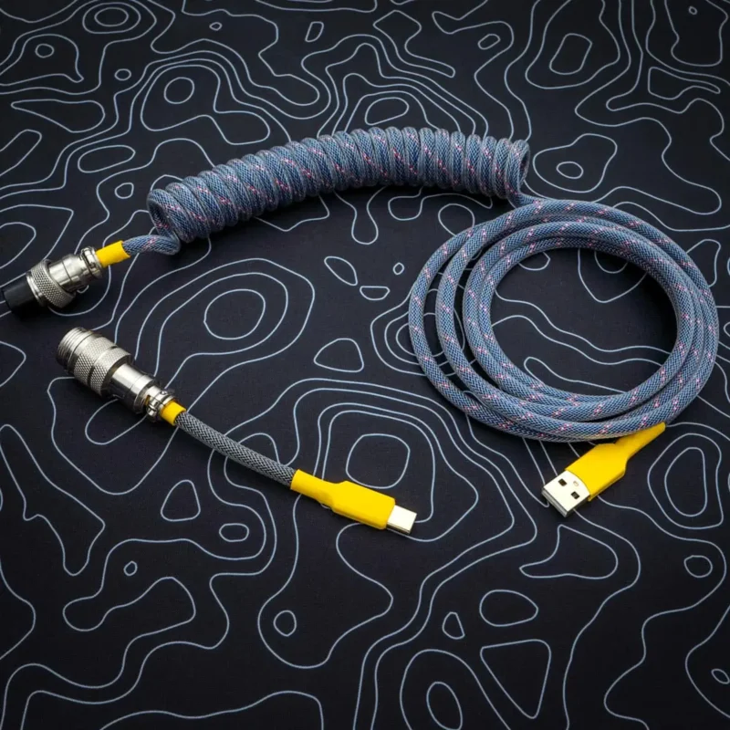 Coiled dark blue keyboard cable with yellow connectors, featuring USB-C and aviator plugs; quality paracord finish with smooth braiding for durability.