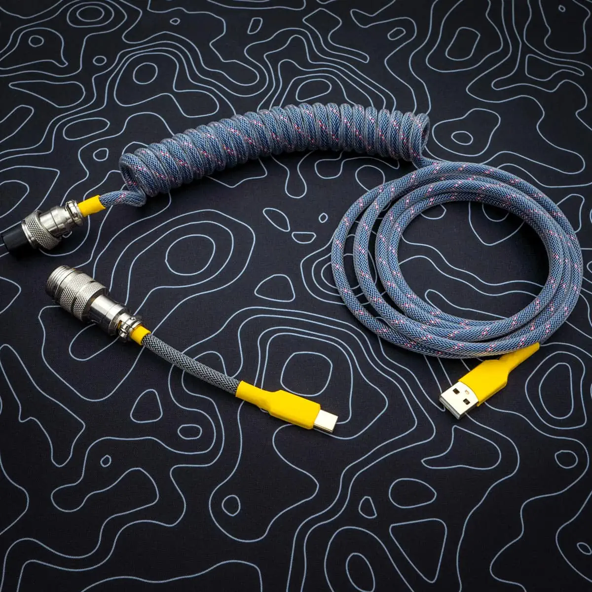 Coiled dark blue keyboard cable with yellow connectors, featuring USB-C and aviator plugs; quality paracord finish with smooth braiding for durability.