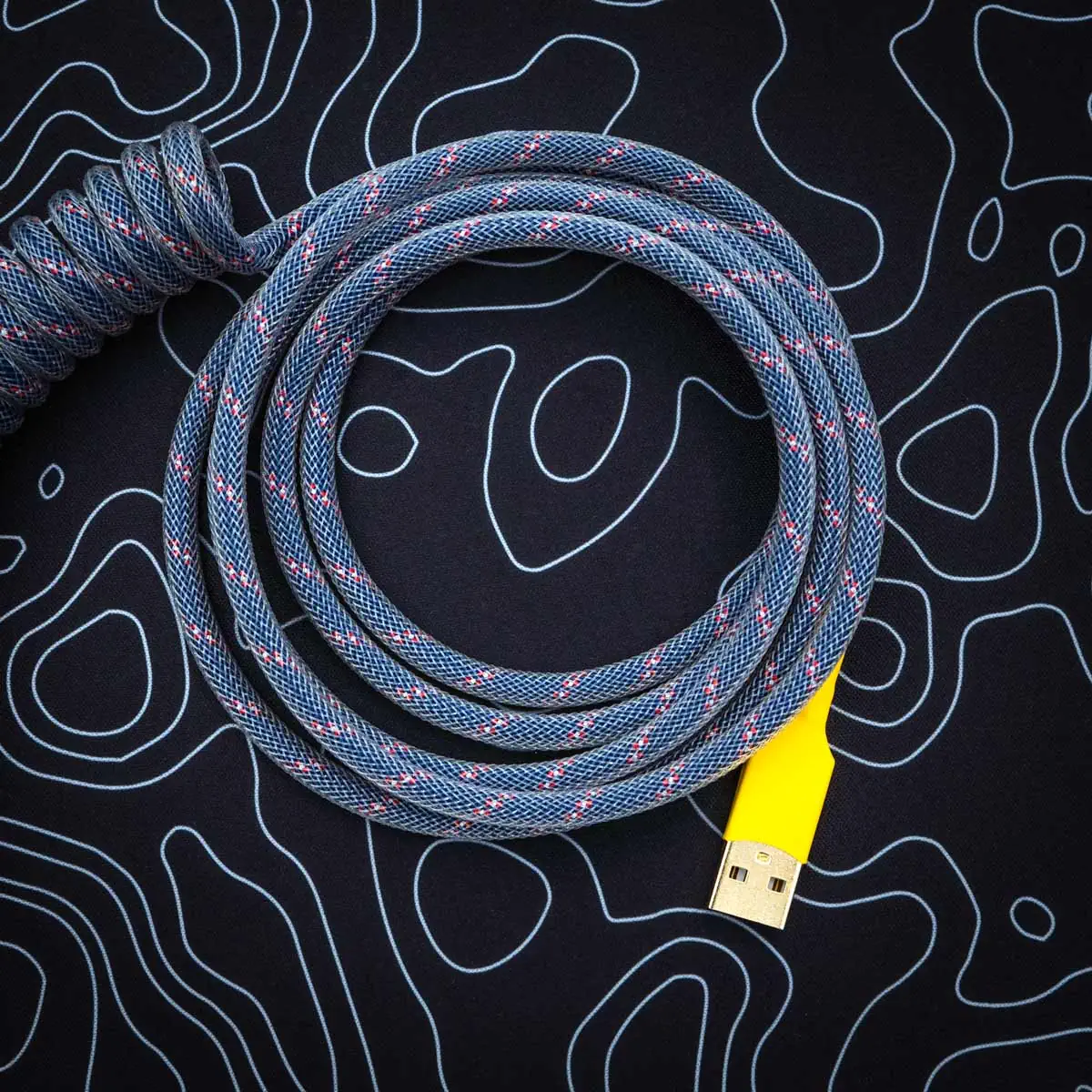 Coiled dark blue paracord keyboard cable with pink accents, featuring a yellow USB connector, ideal for custom setups. Durable and stylish design.