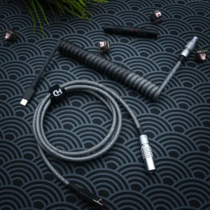 Dark gray keyboard cable featuring a coiled design, USB-C and aviator connectors, durable paracord, and high-quality CNC metal housing for a sleek finish.