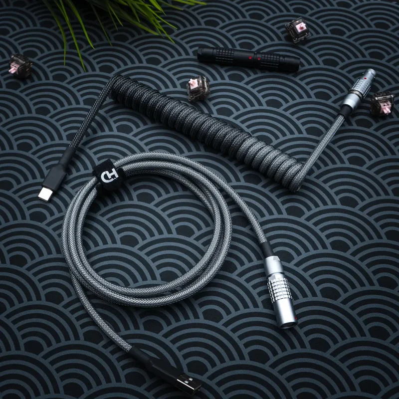 Dark gray keyboard cable featuring a coiled design, USB-C and aviator connectors, durable paracord, and high-quality CNC metal housing for a sleek finish.