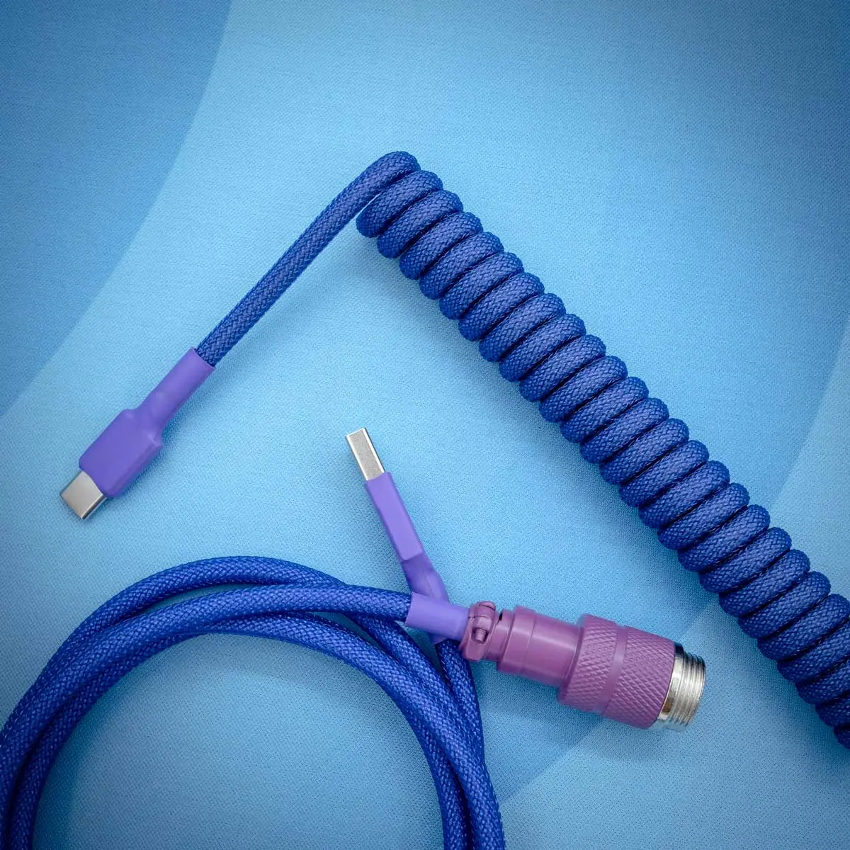 Dark purple, coiled keyboard cable with USB-C and detachable aviator connectors. Features durable paracord, smooth braiding, and quality finish.