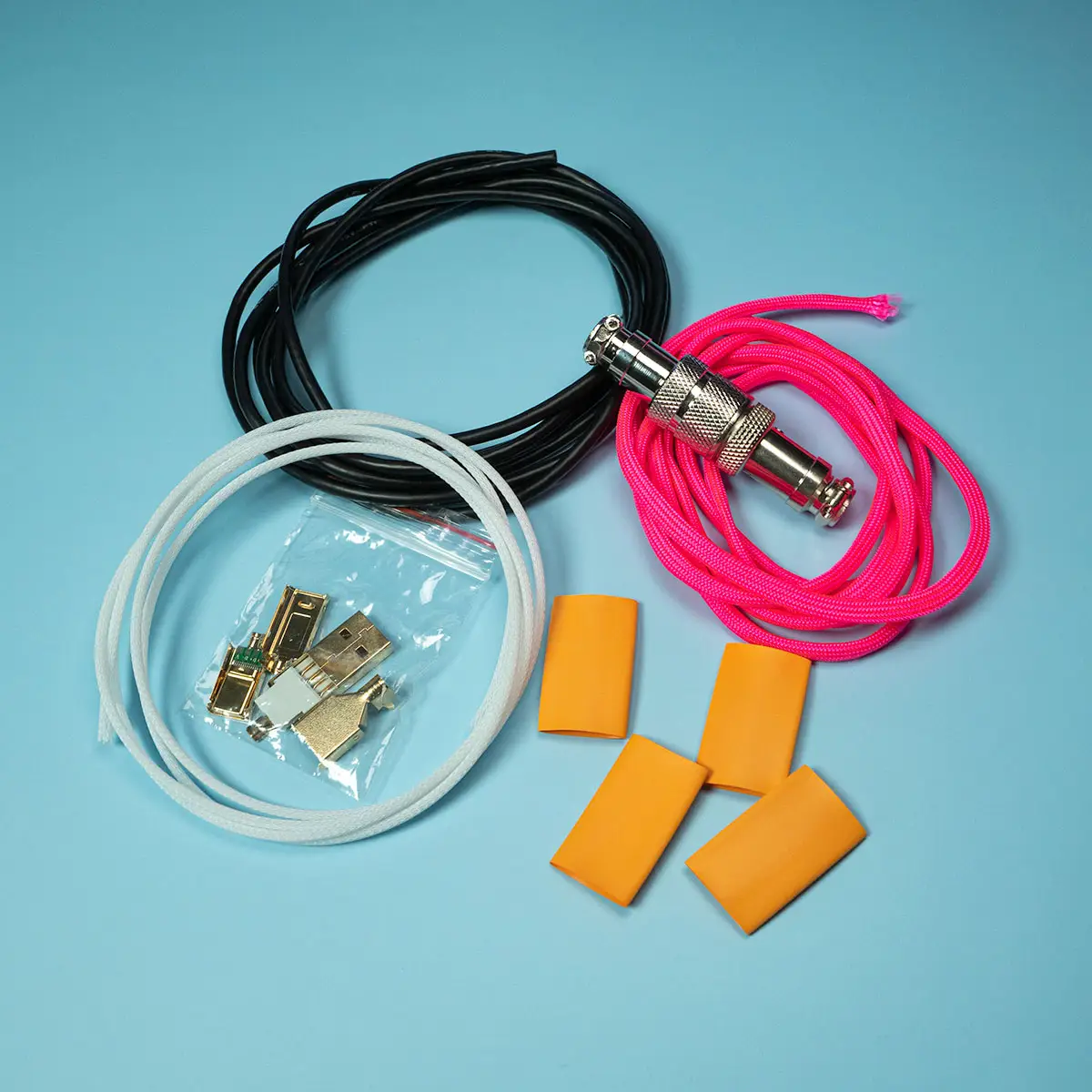 Various cable electronic components, including three colored wires, connectors in a plastic bag, and four orange heat shrink tubes, are arranged on a blue background as part of a DIY USB Cable Kit.