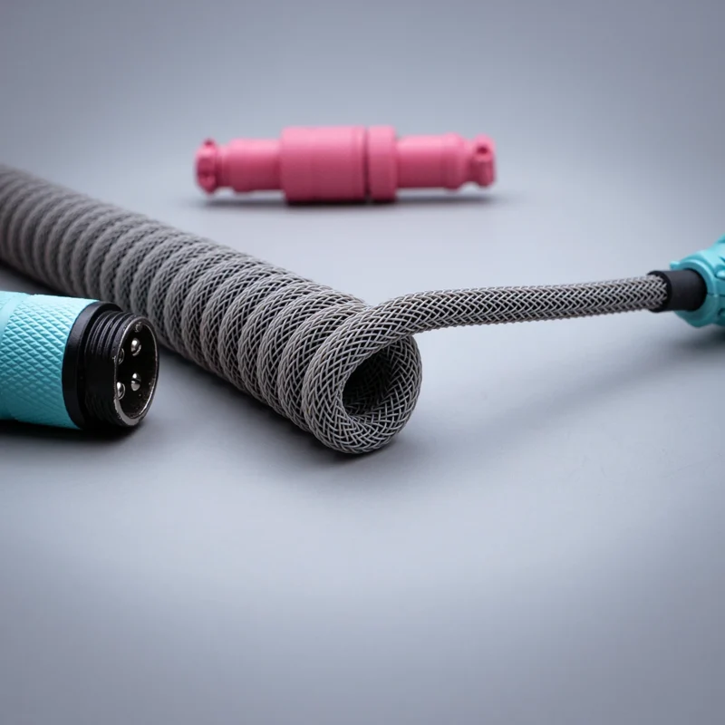 Coiled custom keyboard cable featuring high-quality braid in gray, detachable USB-C and aviator connectors, accented with vibrant pink and teal housing.