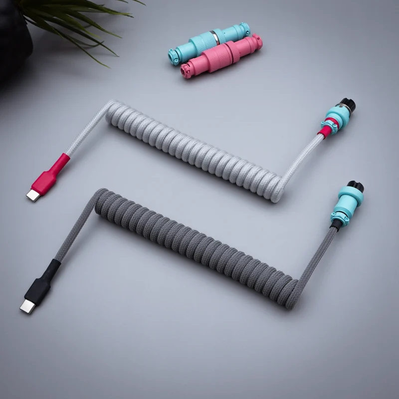 Coiled keyboard cables in gray and metallic finishes, featuring USB-C connectors. Includes detached plugs with vibrant colors and durable braiding.