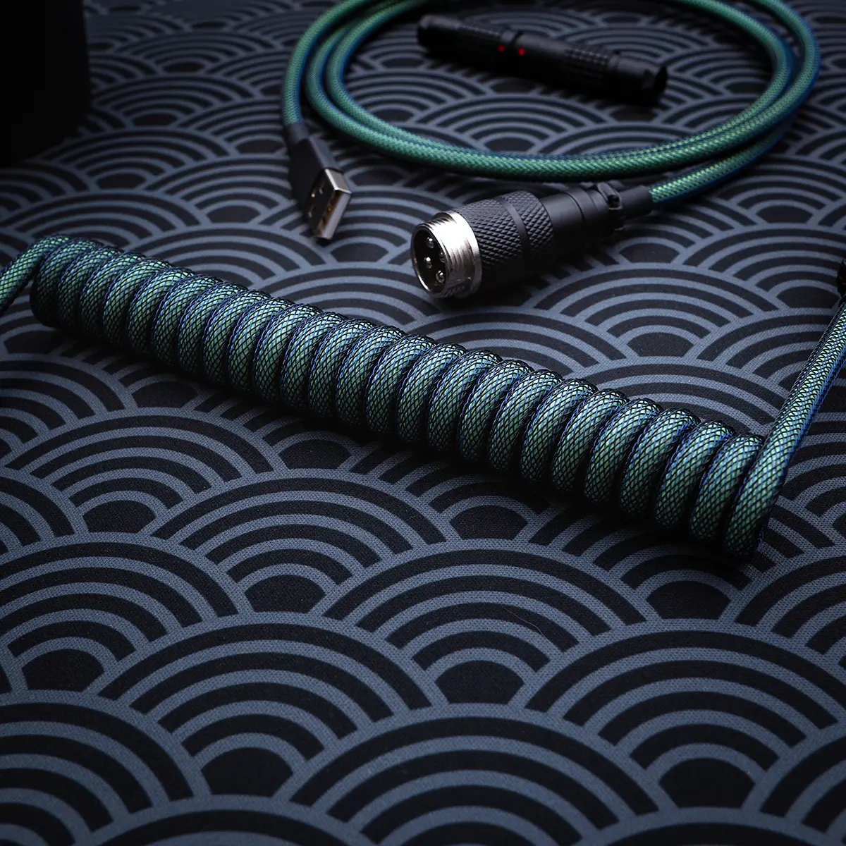 Coiled green keyboard cable with glow-in-the-dark features, USB and aviator connectors, braided techflex, and high-quality CNC metal housing for durability.