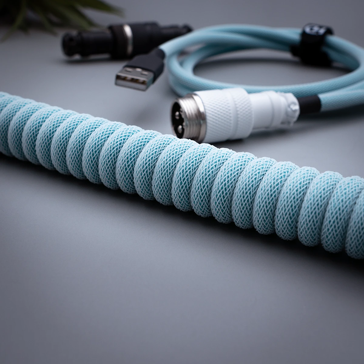 Custom keyboard cable featuring a coiled design in light blue techflex, with USB and aviator connectors and high-quality CNC metal housing for durability.