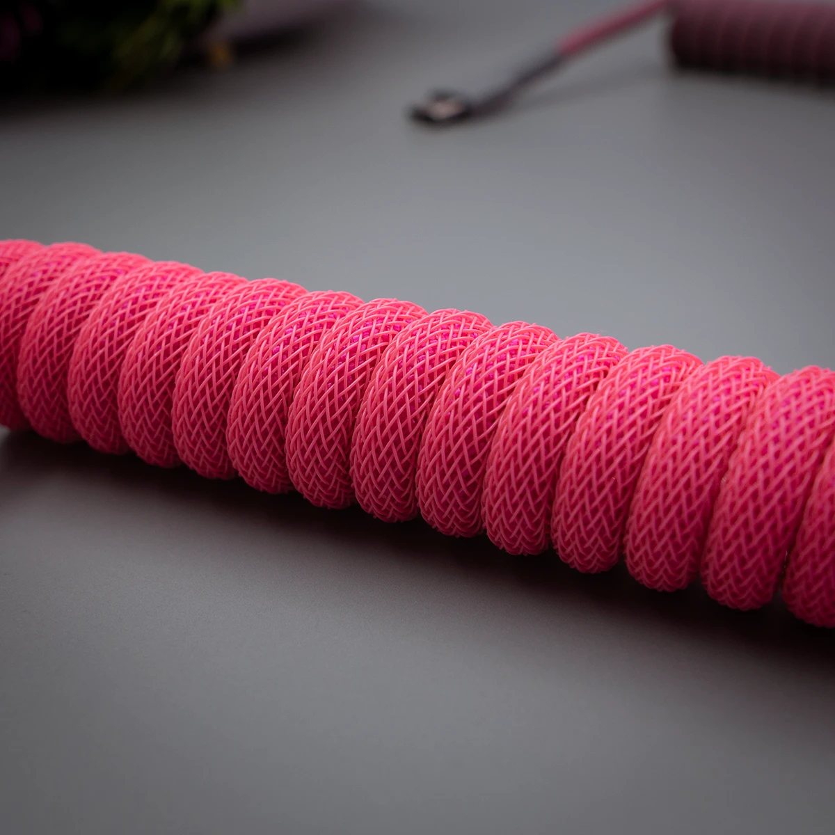 Coiled pink keyboard cable with a textured paracord finish. Features high-quality braiding and durable connectors for a striking, customized look.