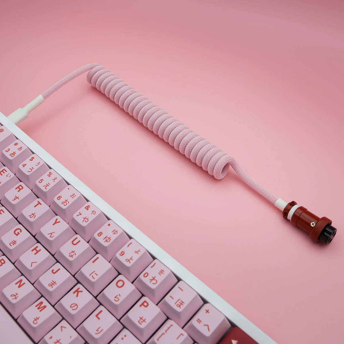 A spiral pink keyboard cable with a soft-paracord finish, featuring a detachable aviator connector for flexible connections.