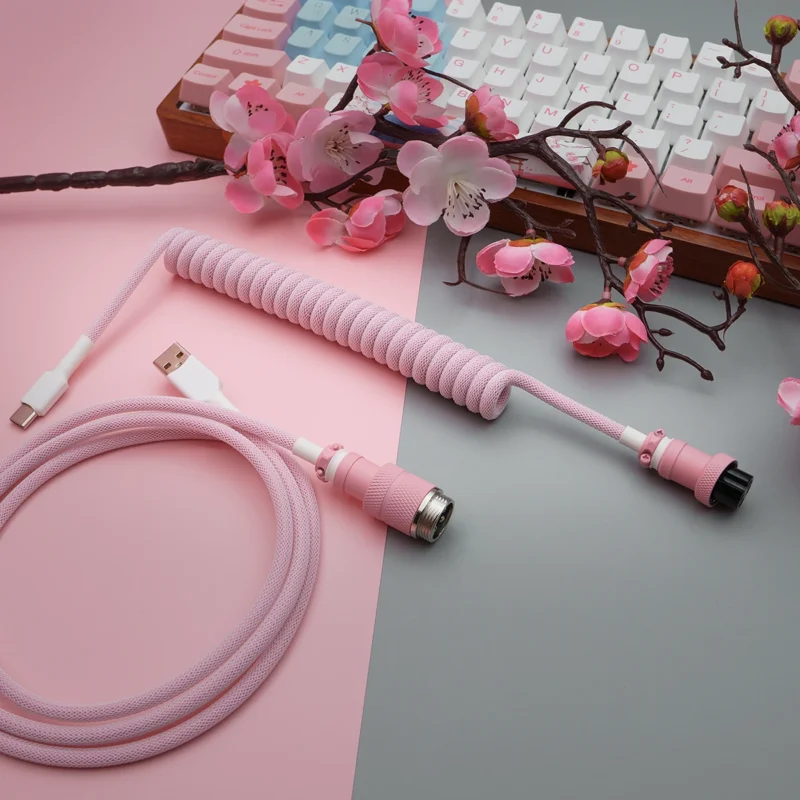Coiled pink paracord keyboard cable with USB-C and aviator connectors, featuring quality braiding, detachable plugs, and stylish heatshrink details.