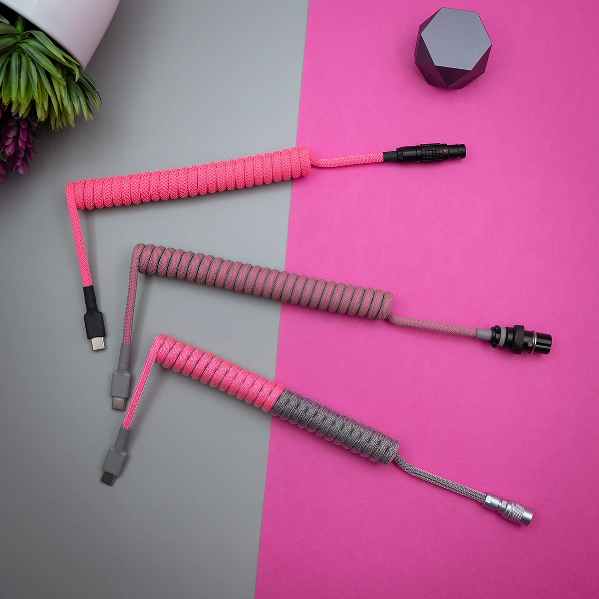 Three custom keyboard cables display vibrant pink and gray paracord braiding. Connectors include USB-C and aviator options, showcasing quality craftsmanship.