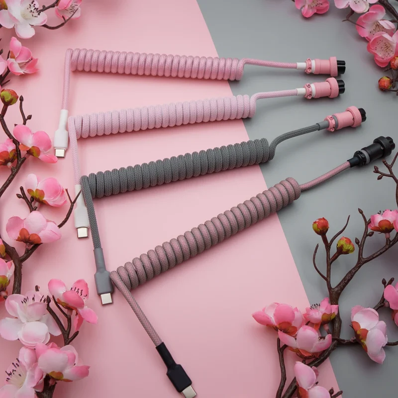 A stylish array of coiled keyboard cables in pink and gray, featuring USB-C connectors, detachable plugs, and premium braiding for durability.