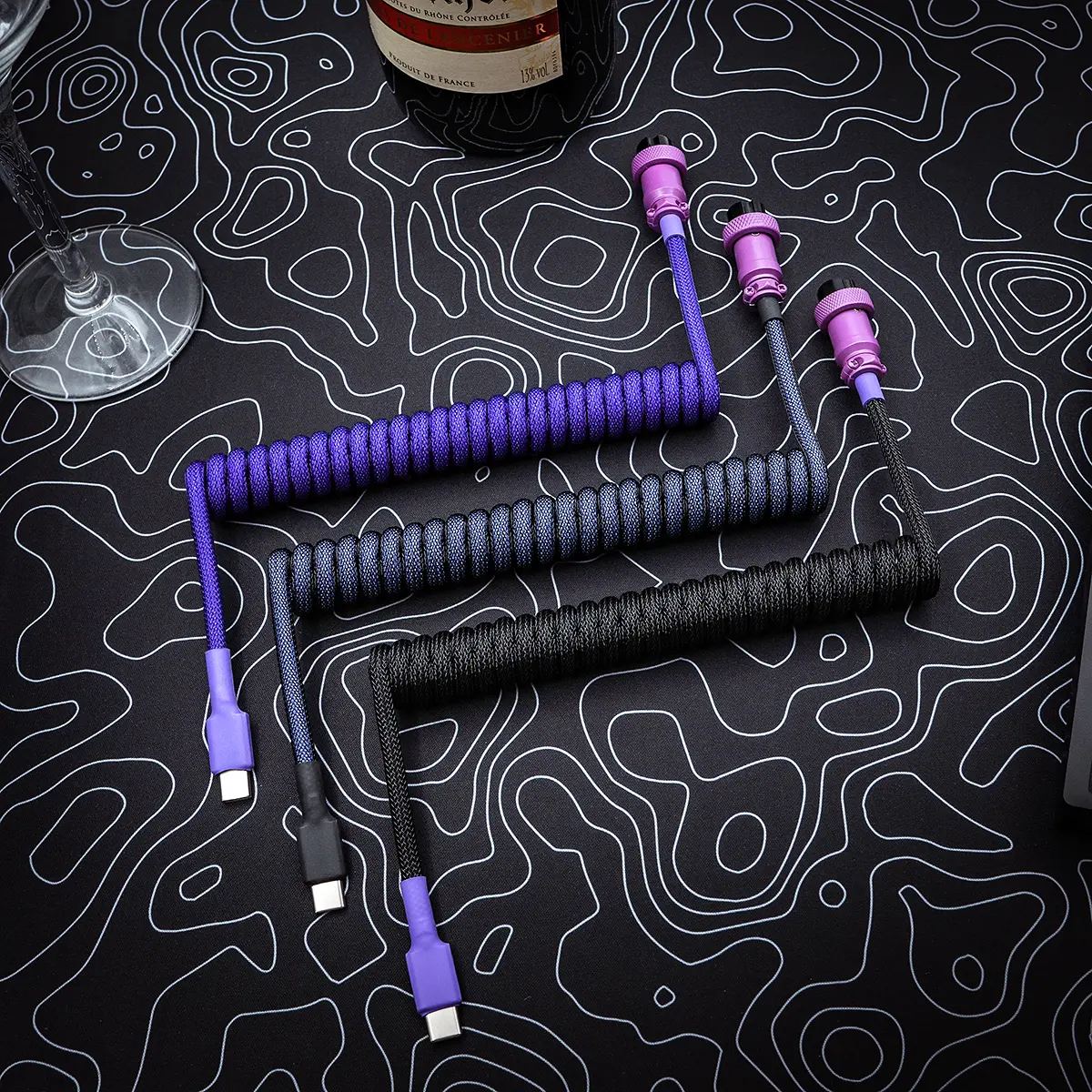 Coiled custom keyboard cables in purple and black, featuring USB-C connectors, detachable plugs, a techflex finish, and high-quality braiding.