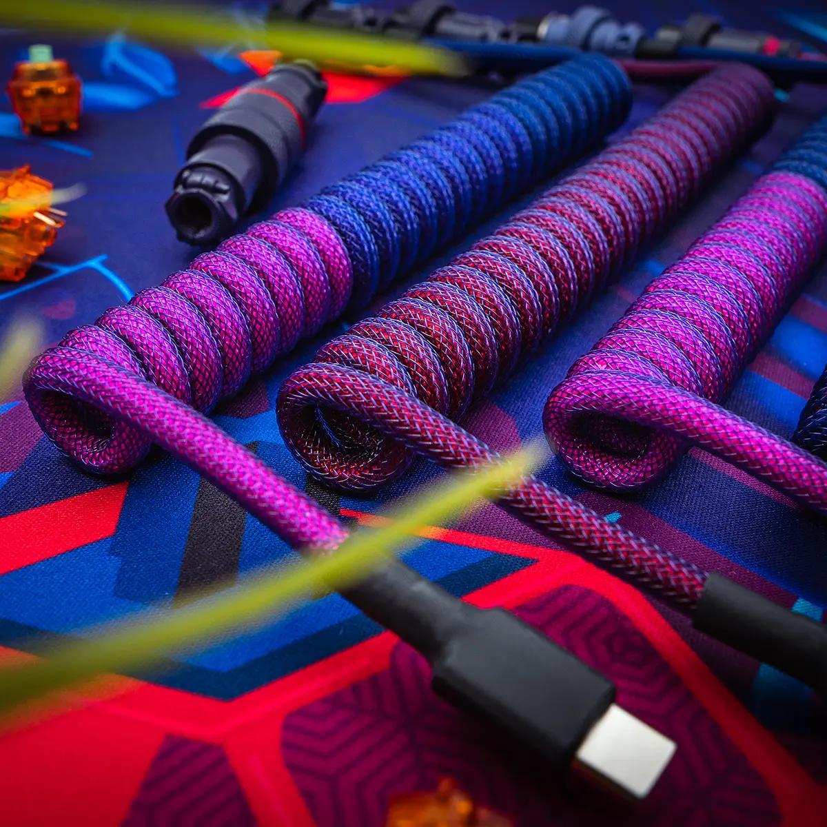 Three coiled custom keyboard cables showcase vibrant color schemes in purple and blue paracord. Features include USB-C connectors and high-quality braiding.