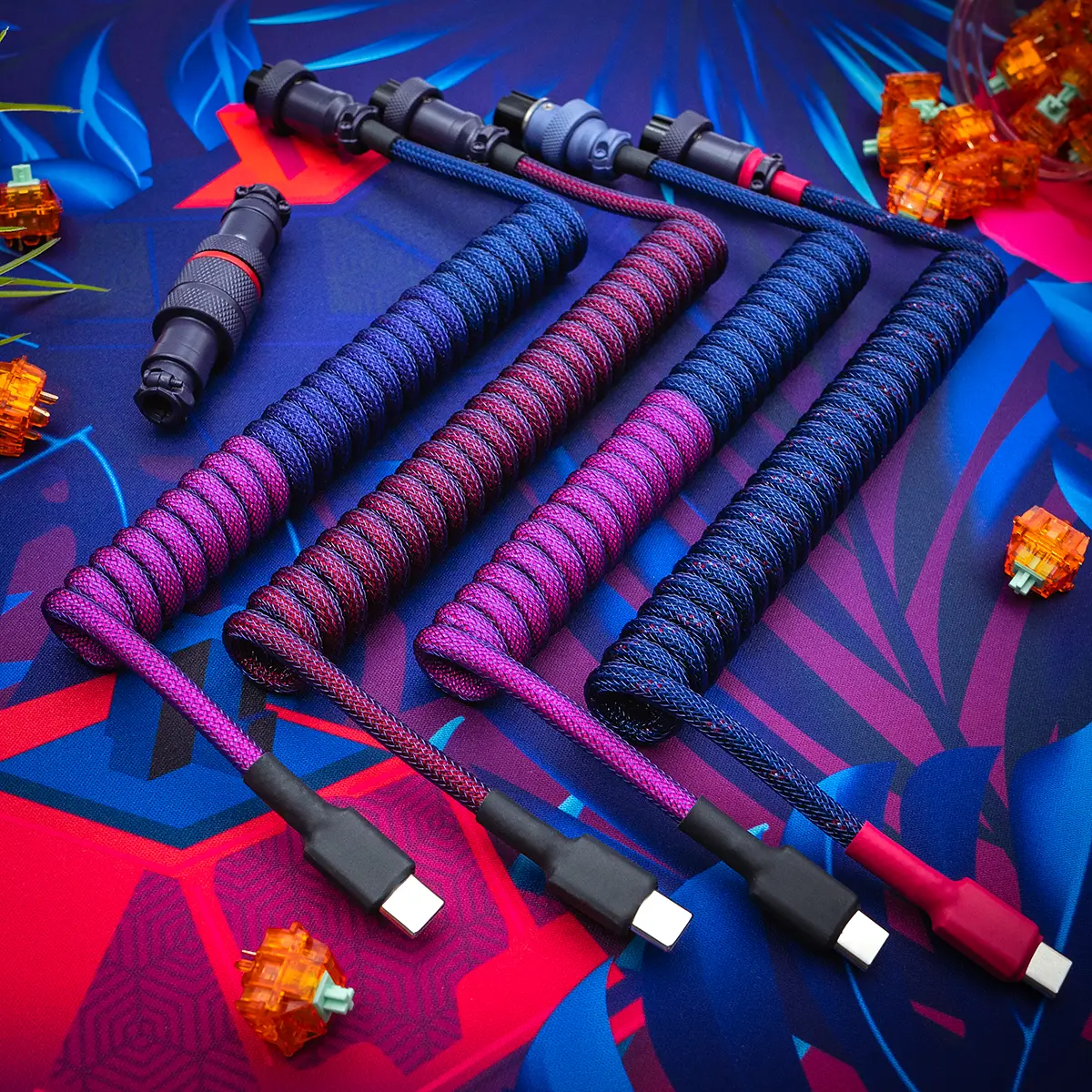 Four custom keyboard cables displayed, featuring vibrant paracord and techflex braiding. Each cable has a coiled section, flat connector ends (USB-C and micro-USB), and detachable plugs for easy use.