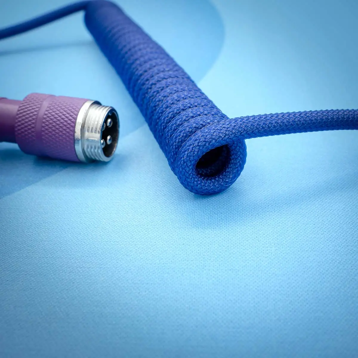 Dark purple keyboard cable with a coiled design, featuring a detachable aviator connector, durable paracord, and high-quality braiding for flexibility.