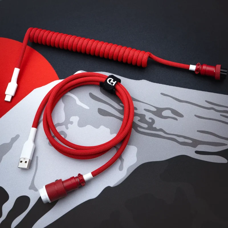 A vibrant red GMK Jamon cable features a coiled design with a USB-C connector and a detachable aviator plug, showcasing premium paracord braiding and heatshrink.