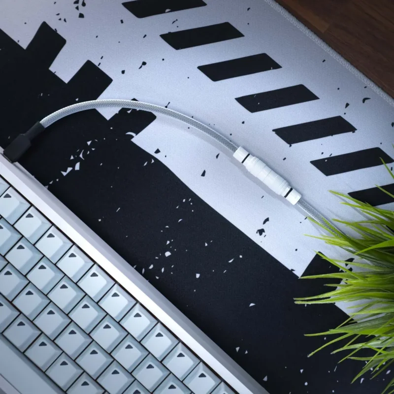 A close-up of a white mechanical keyboard, a braided cable with a YC8 connector, and green artificial grass on a black-and-white patterned desk mat.