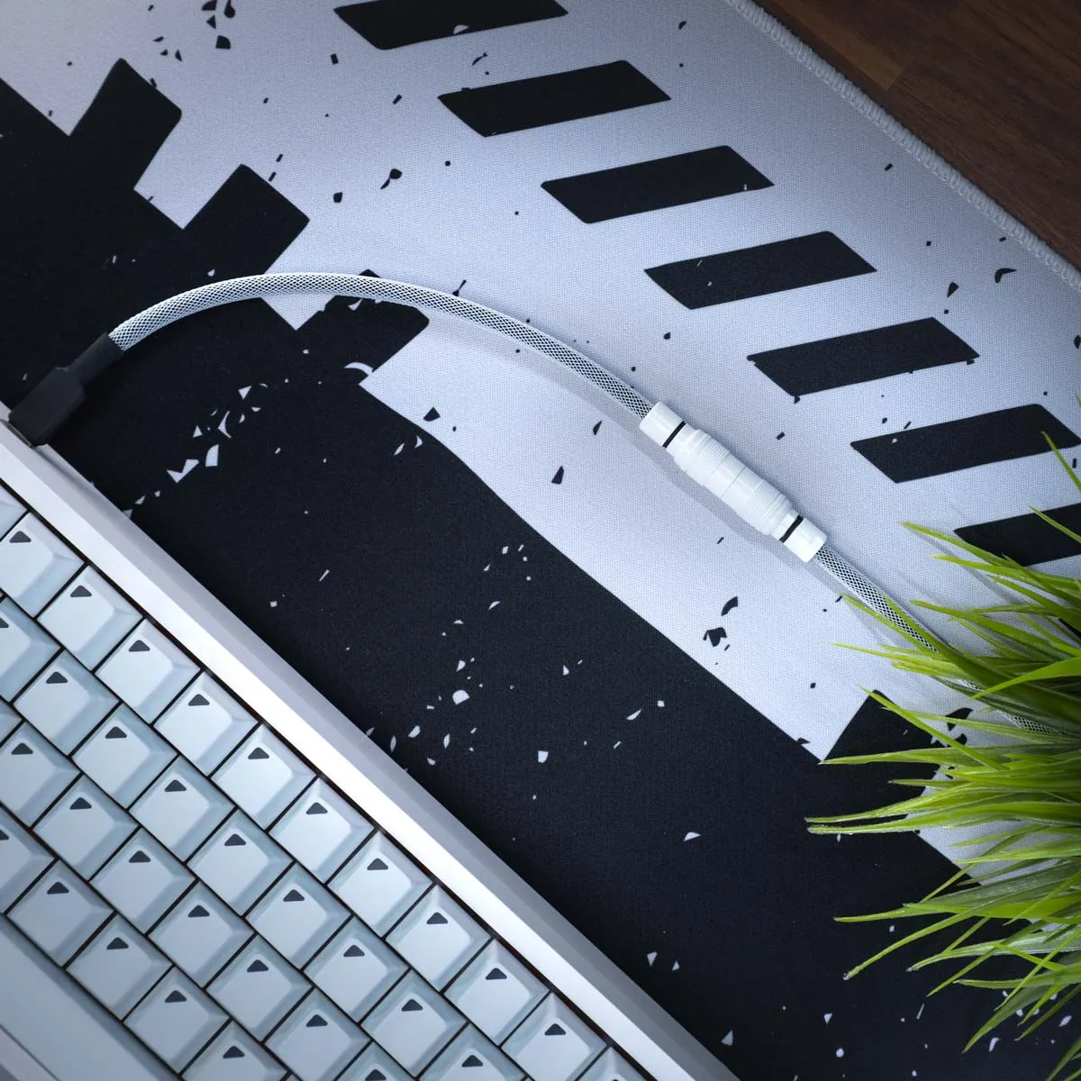 A close-up of a white mechanical keyboard, a braided cable with a YC8 connector, and green artificial grass on a black-and-white patterned desk mat.
