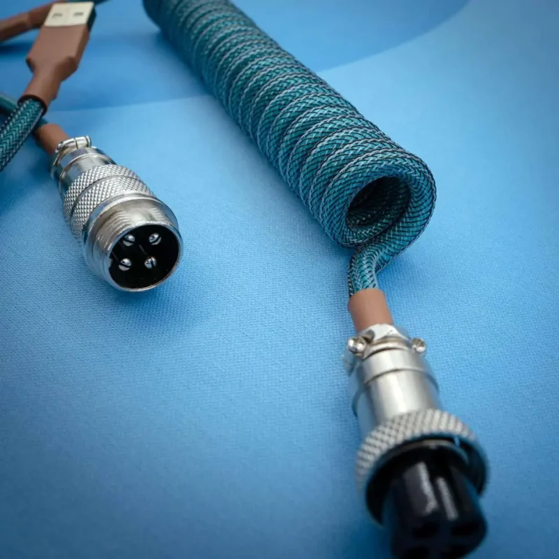 Coiled blue-green paracord keyboard cable with detachable connectors, featuring USB and AVIATOR ends, showcasing high-quality braiding and metal housing.