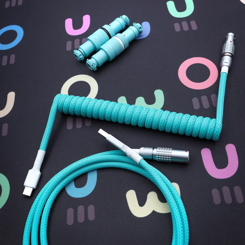 A vibrant turquoise coiled keyboard cable featuring detachable USB-C and aviator connectors, wrapped in a durable, textured braid for stylish functionality.
