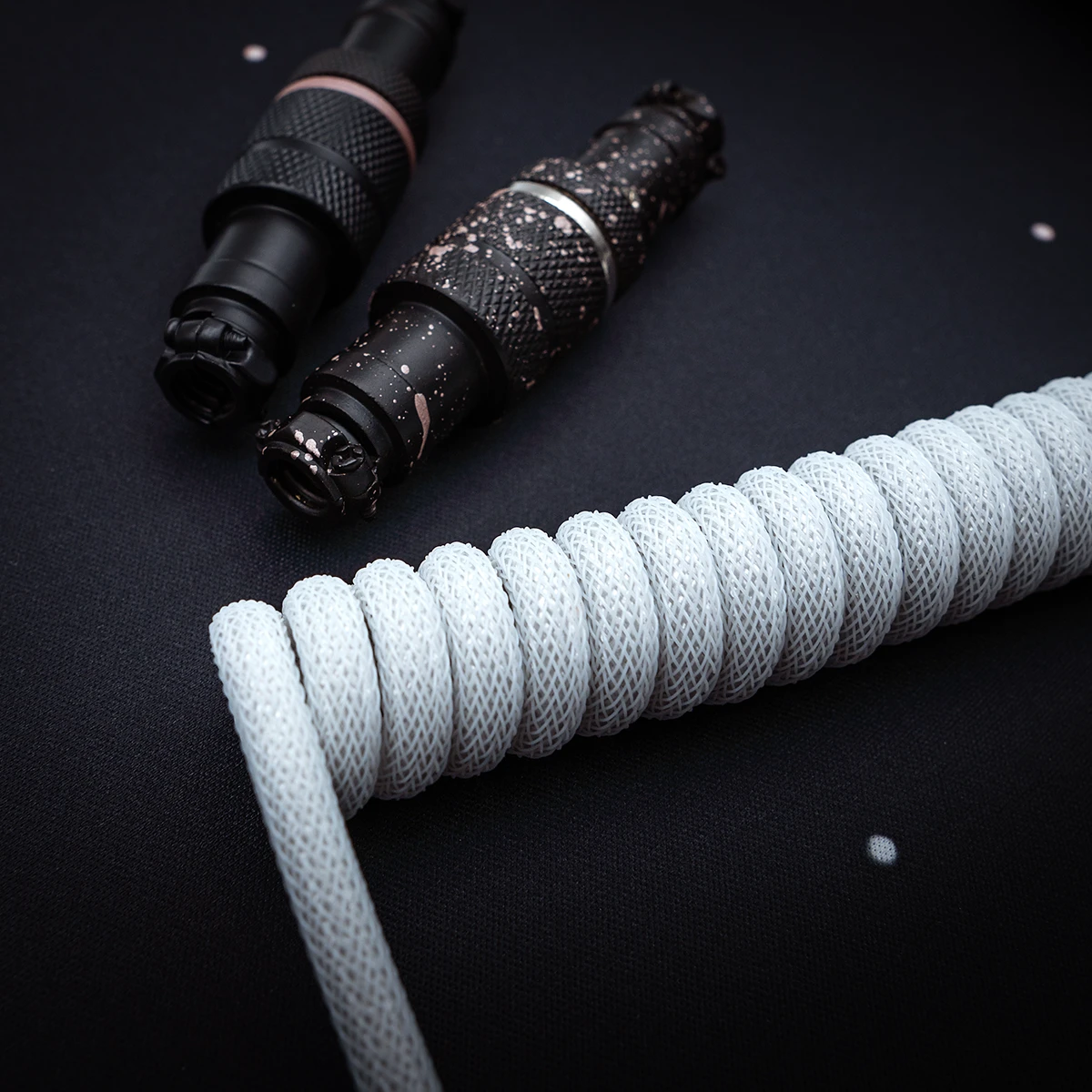 Coiled white paracord keyboard cable with textured connectors in black and pink accents. Features extendable sections and detachable plugs for versatility.