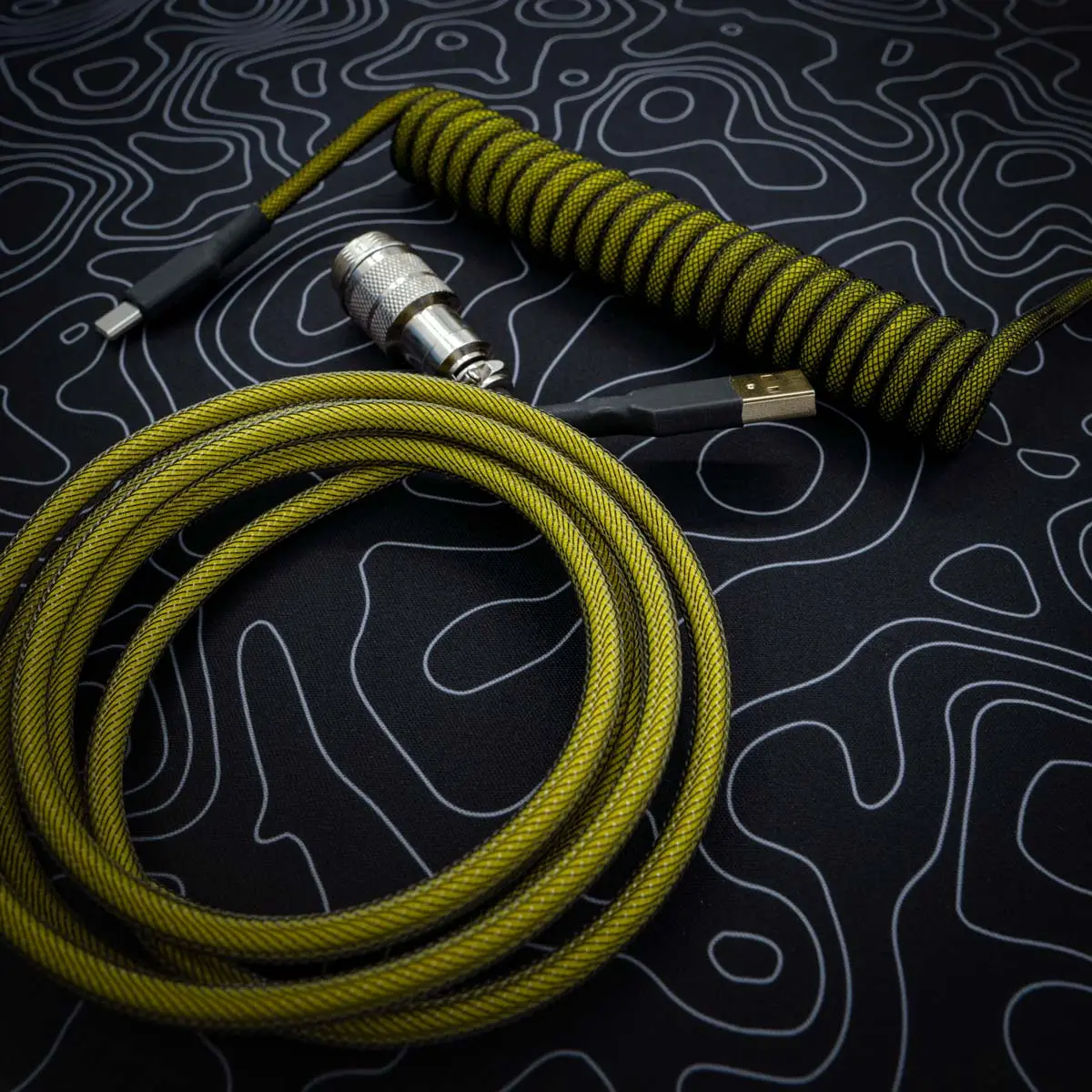 Coiled yellow and black keyboard cable featuring USB-C and detachable metal aviator connectors. Durable paracord finish with a sleek braided design.